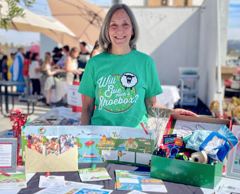 Woman standing behind table of Operation Christmas Child supplies.