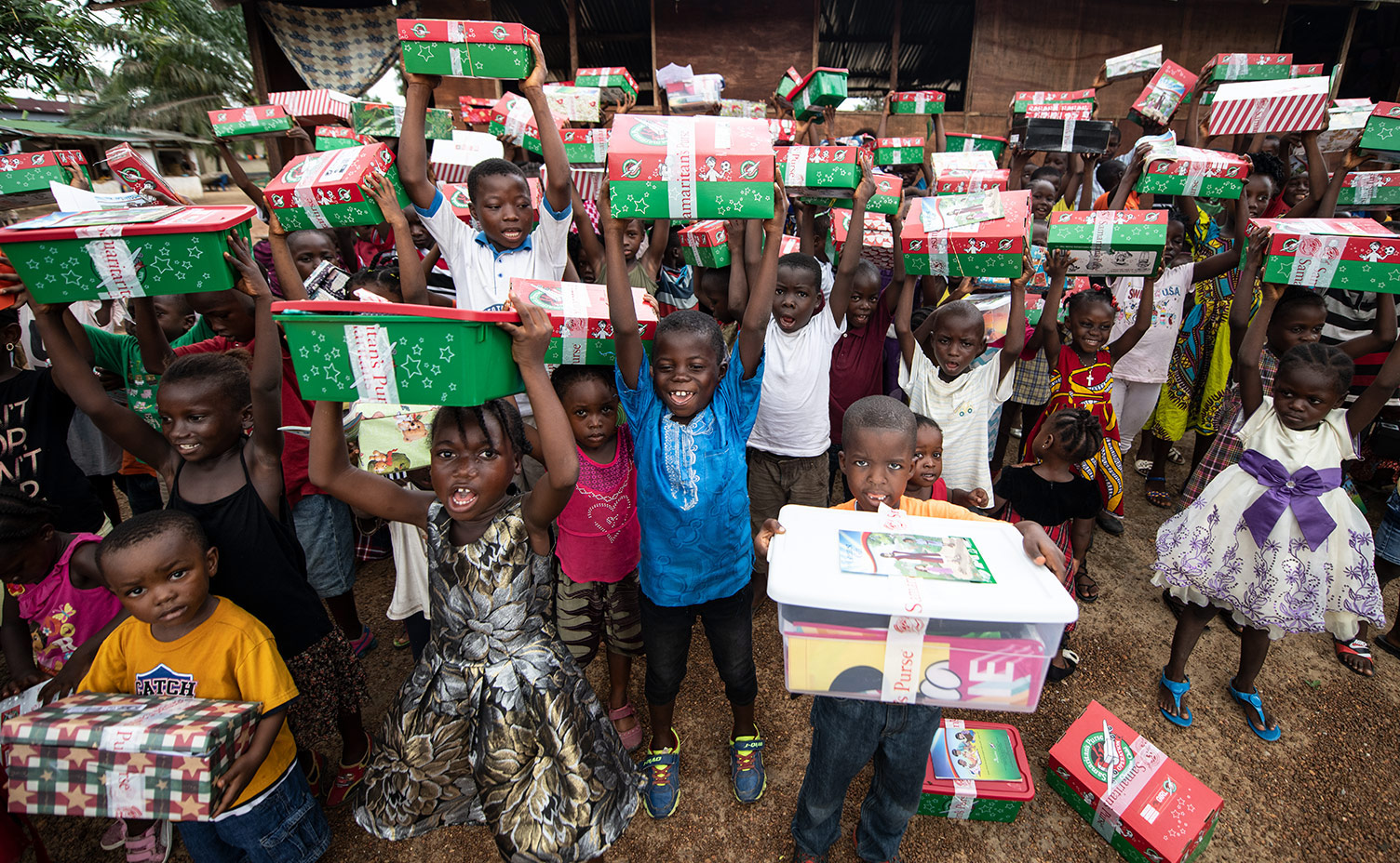 Children hold their Operation Christmas Child Shoeboxes high above their heads.