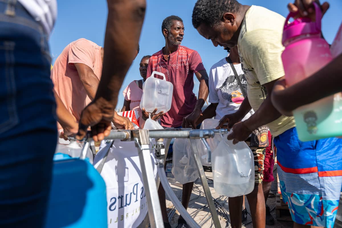 A man retrieving water from a water pump with a crowd of people.