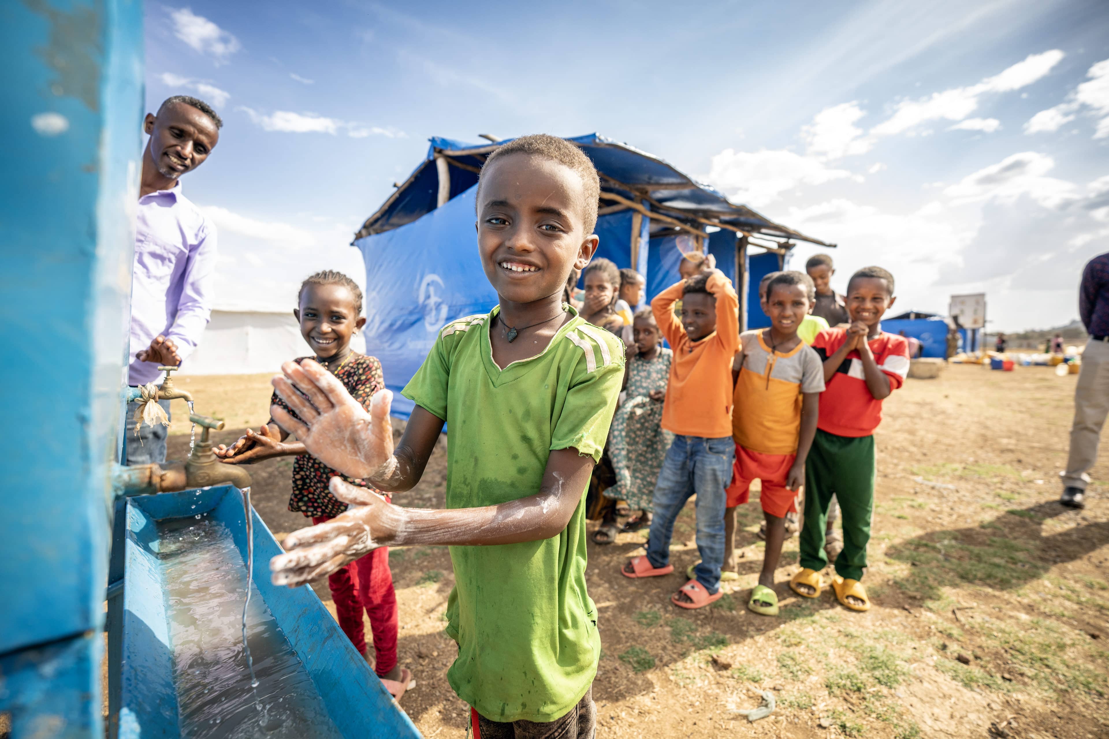 Boy washing his hands amongst a group of children.
