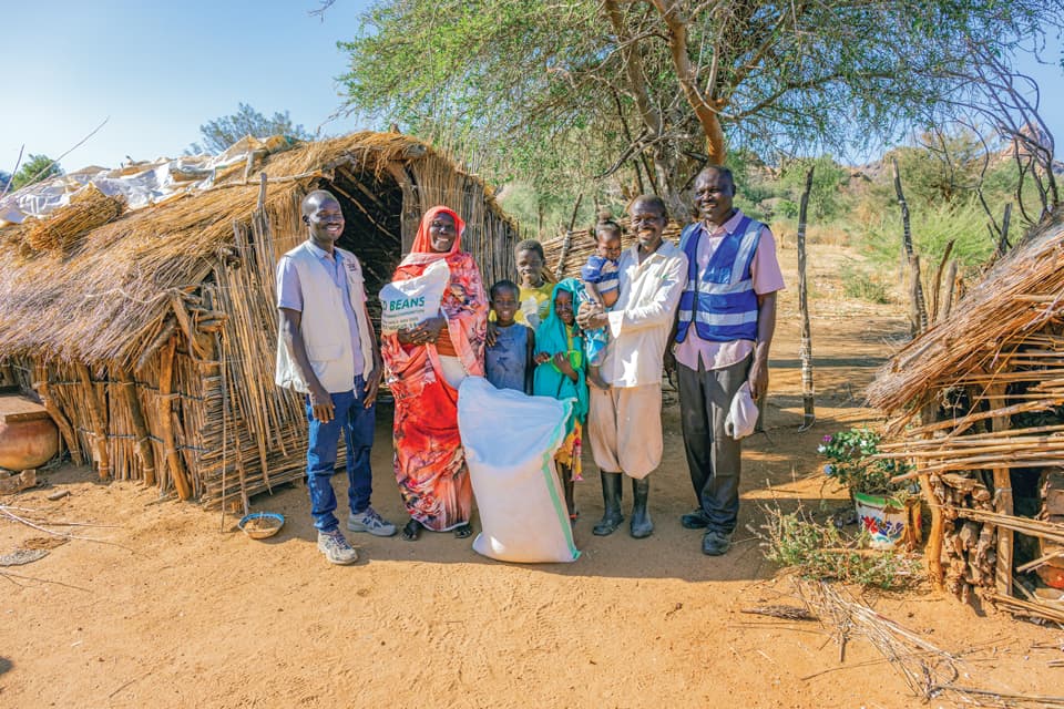 A group of people holding a bag of food in front of some huts.