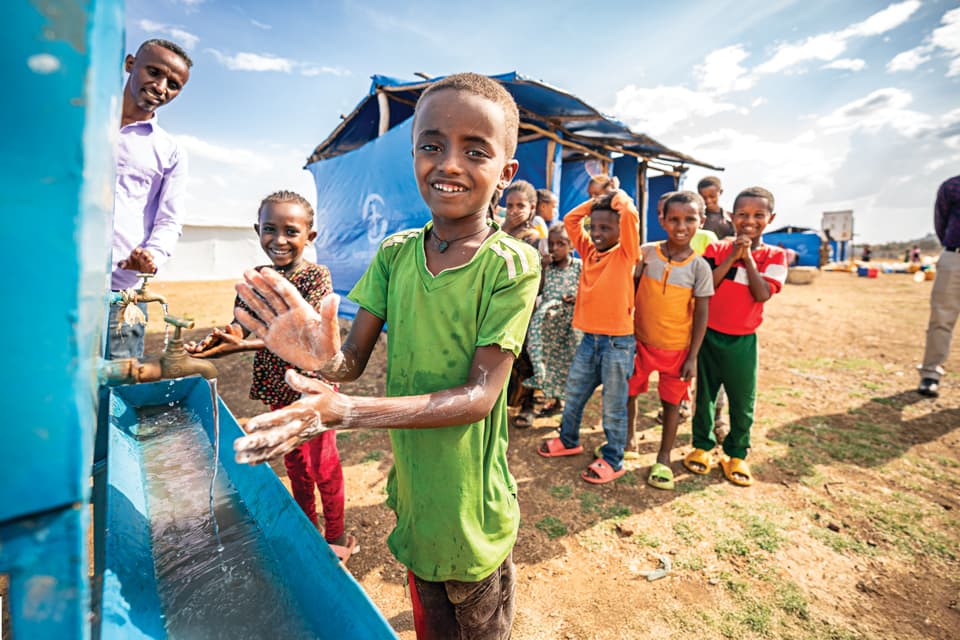 Boy washing his hands amongst a group of children.