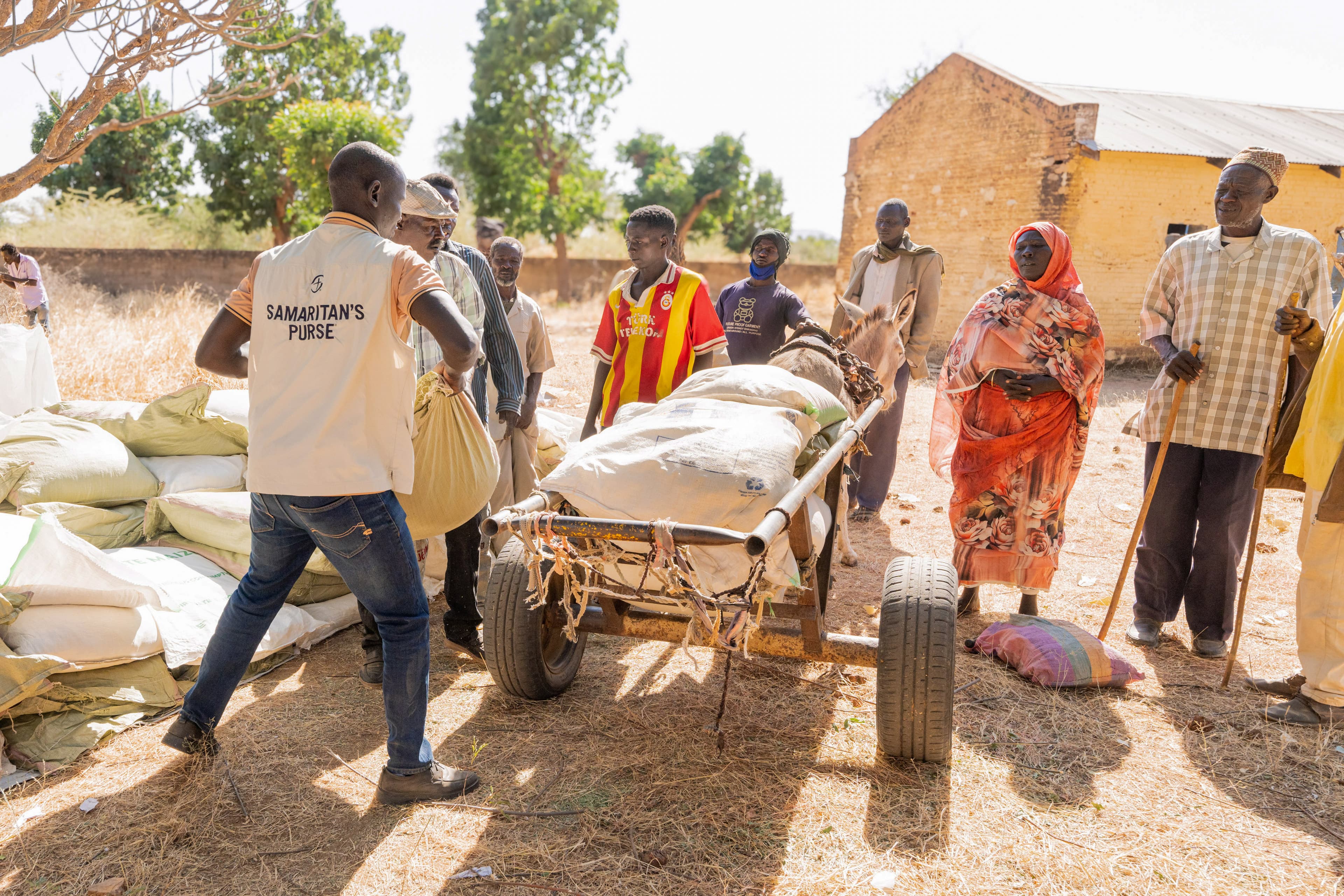 Man loading cart behind donkey with food supplies.