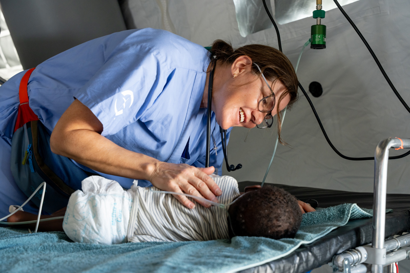 A woman taking care of a baby on a bed.