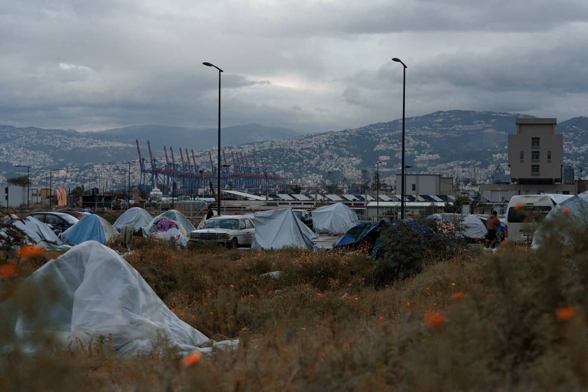 Many tents and cars in front of a mountain.