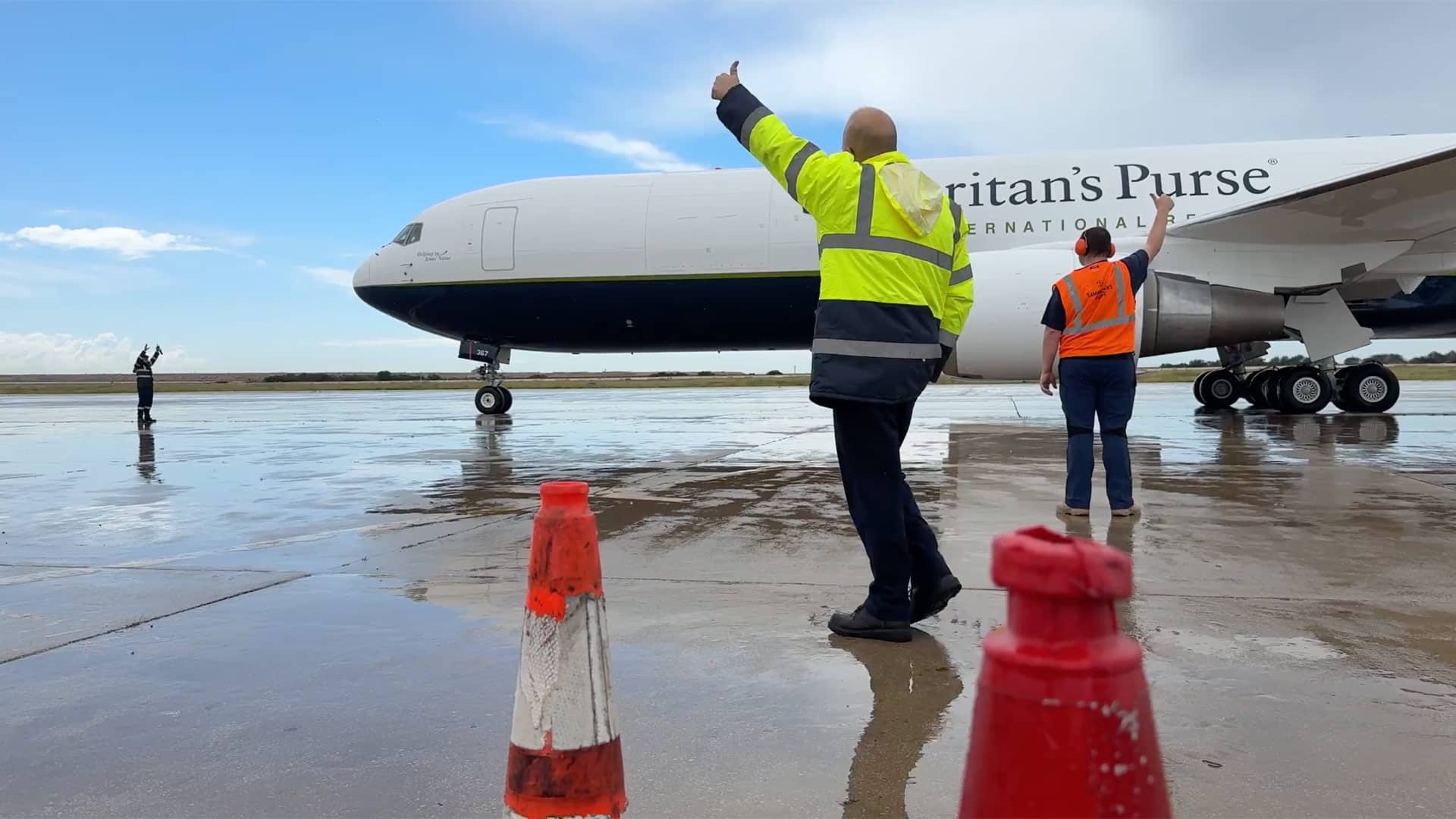 Two people putting their thumbs up in front of an airplane.