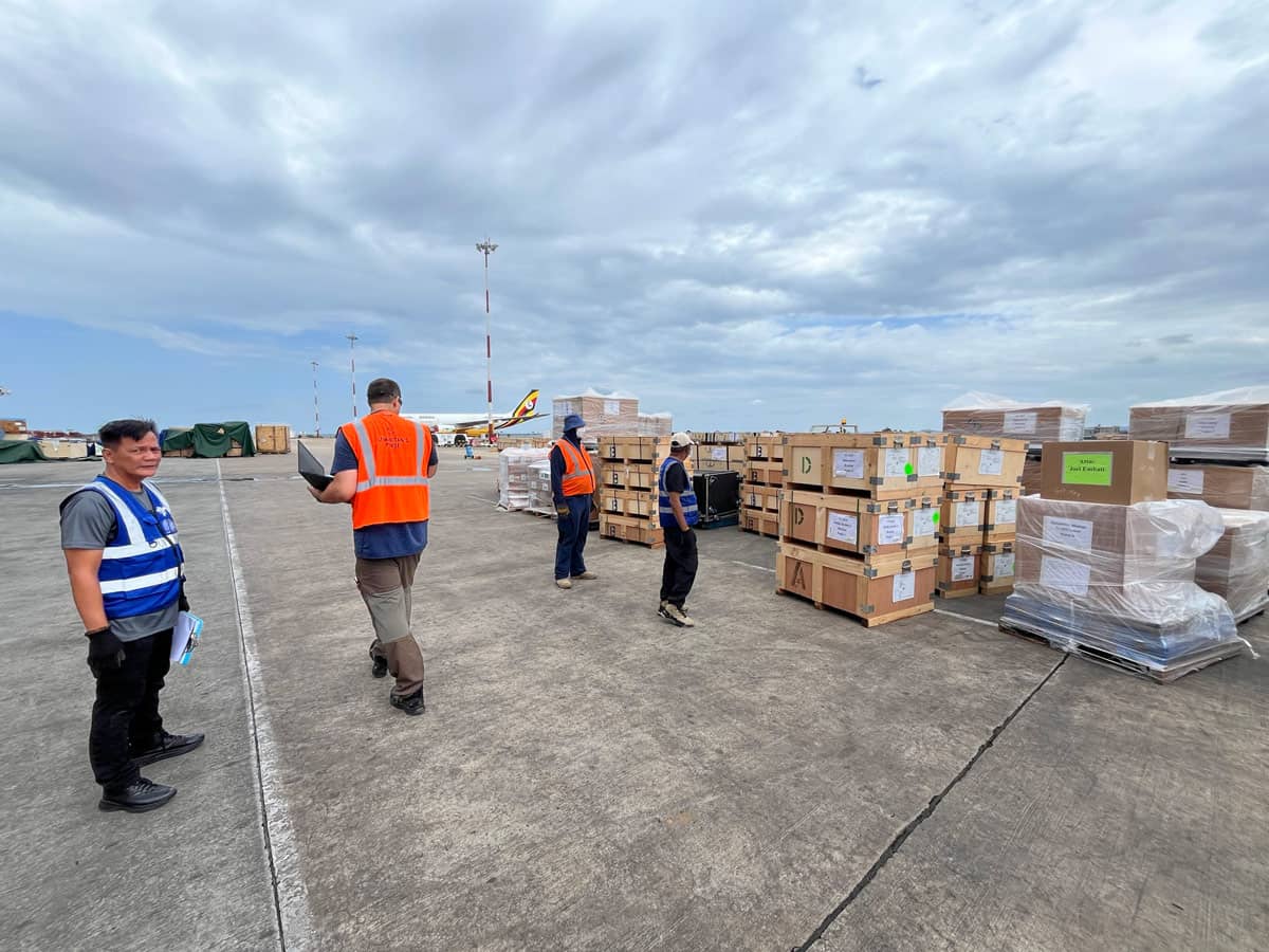 A group of workers in vests standing in front of crates of supplies.
