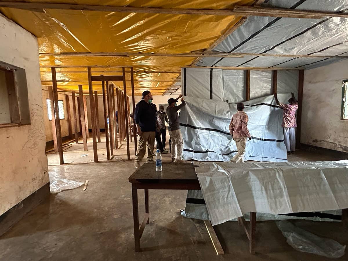 People putting large plastic tarps onto the walls and ceilings in a building.