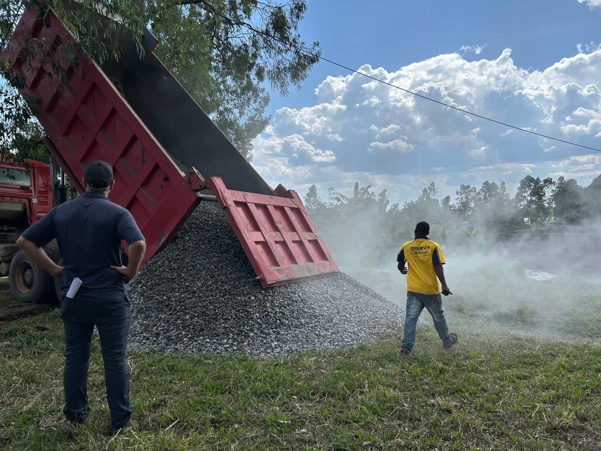 A truck dumping large amount of gravel on the ground. Two people standing in front of the gravel.