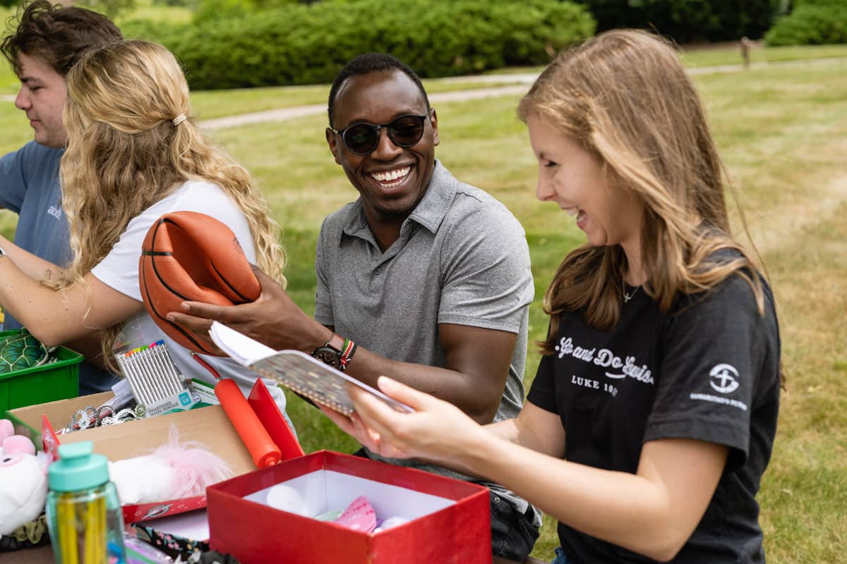 A group of young adults putting gifts into shoeboxes on picnic bench.