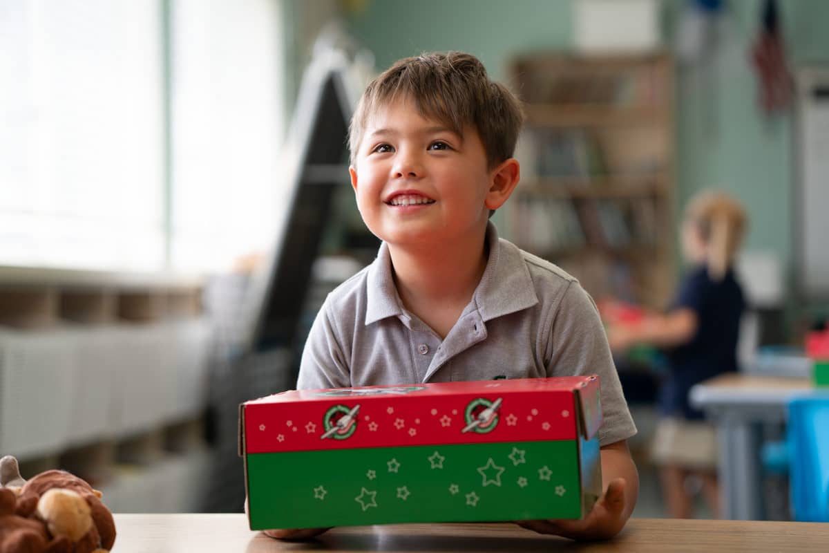 Boy smiling while holding shoebox gift.