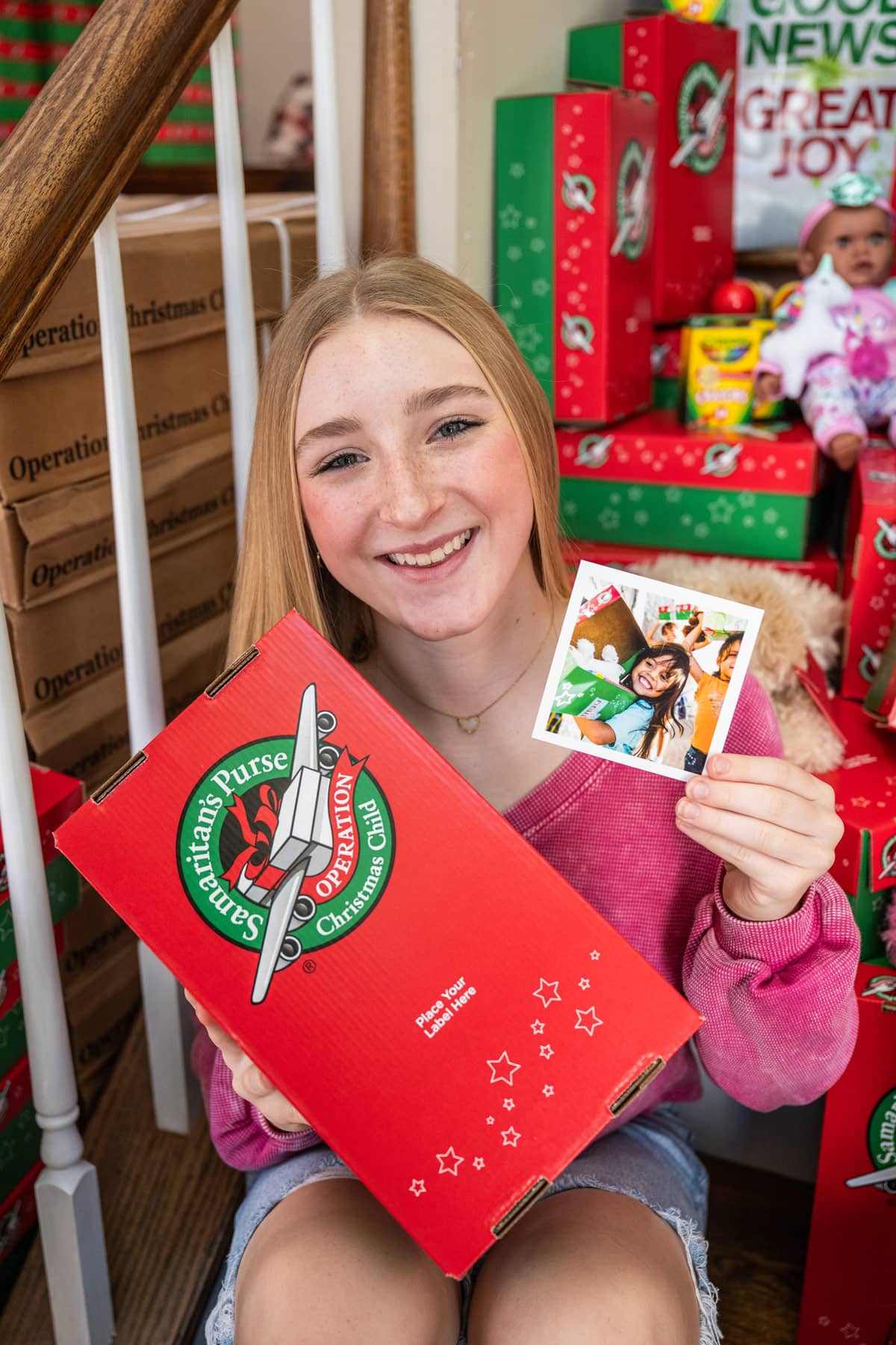 Young girl smiling while holding shoebox gift and picture.
