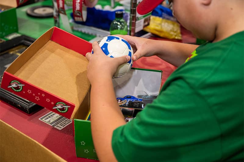 Boy putting a soccer ball toy inside a shoebox gift.