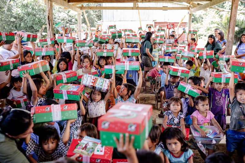 A large group of children holding shoeboxes above their heads in excitement.