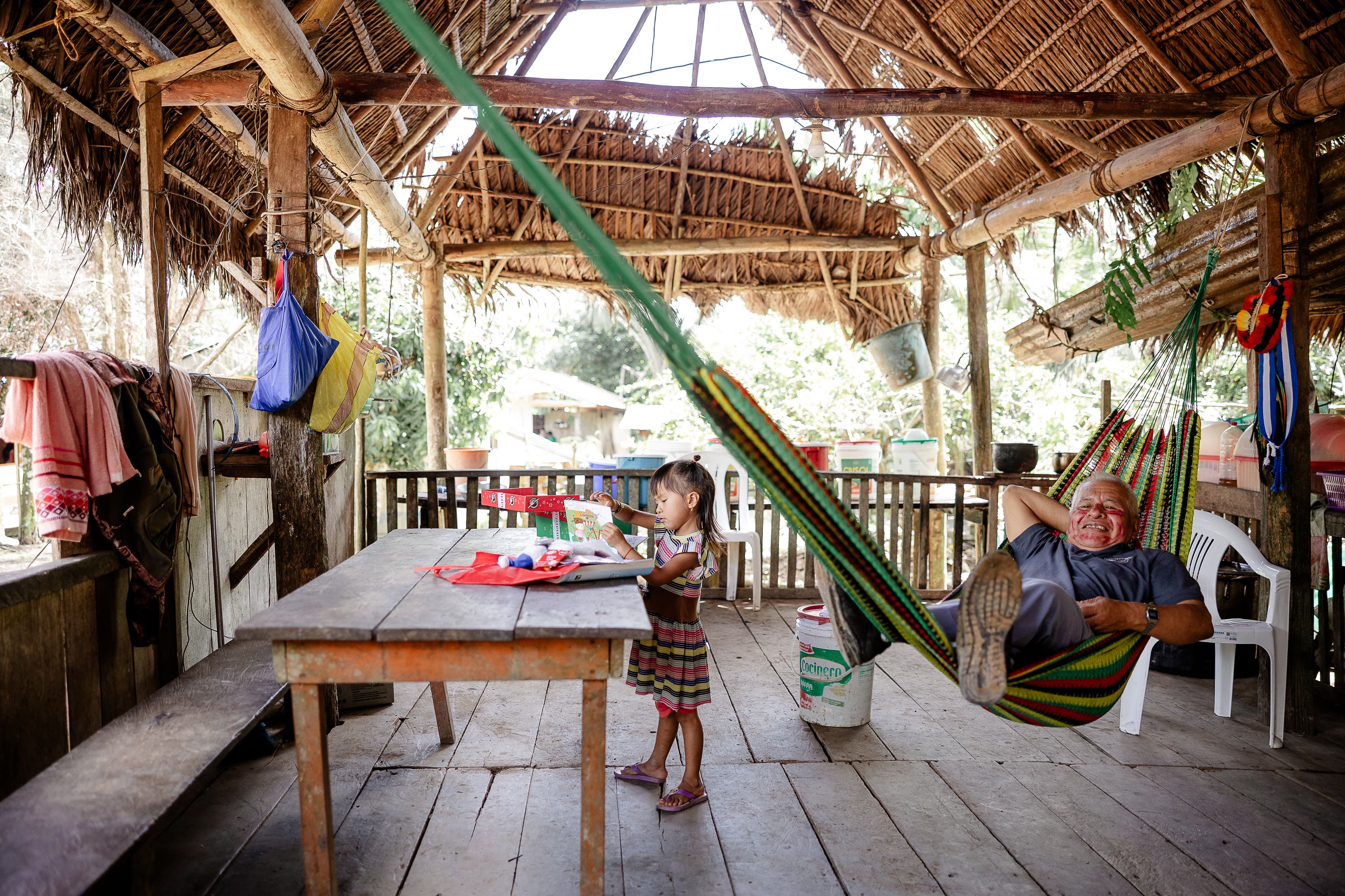A little girl going through her shoebox gift while a man lays in a hammock to her right.