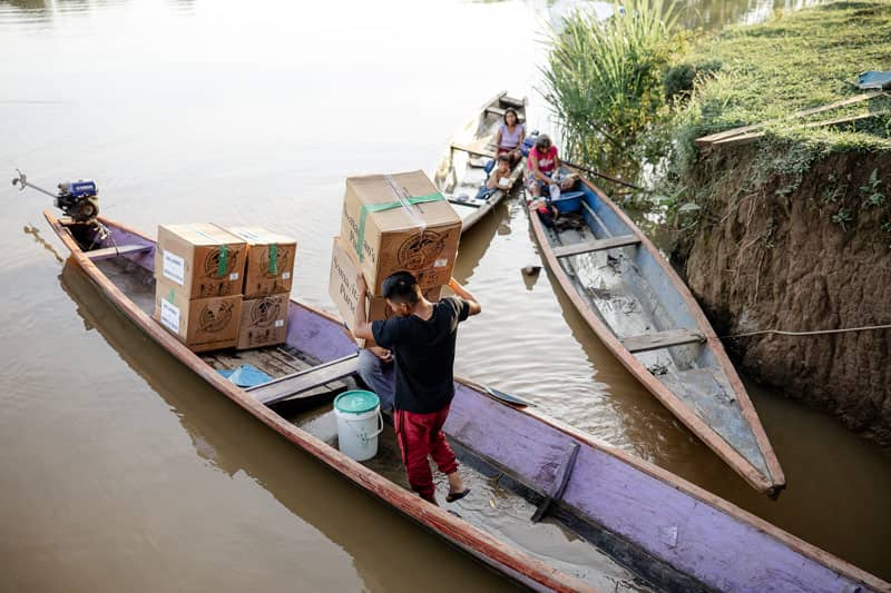 A man carrying large boxes into a canoe on the river.