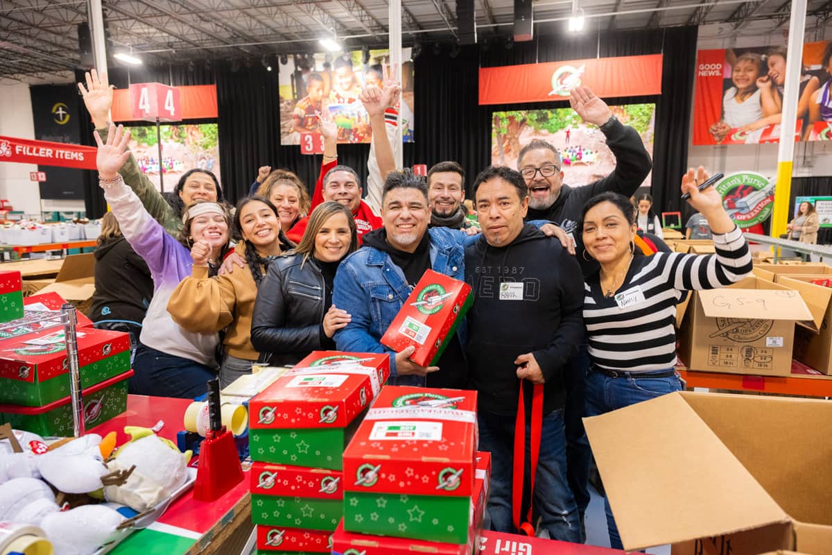 A group of people smiling with holding a shoebox gift in a facility.