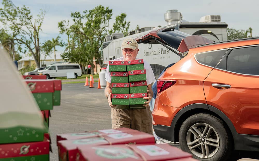 A man walking with shoeboxes in his hands.