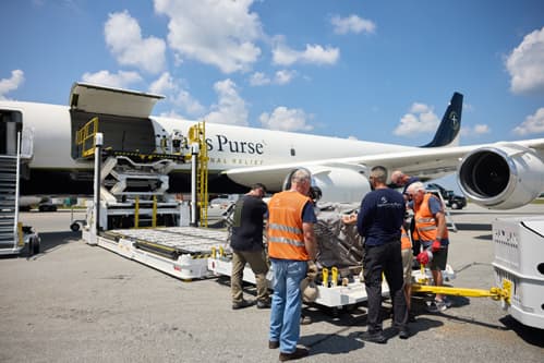 Group of workers praying over cargo with plane in the background.