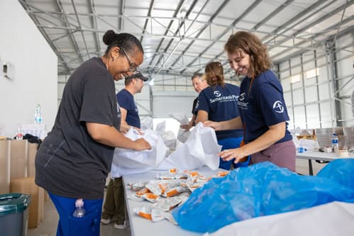 Two  women loading food packets into bags with others behind them.