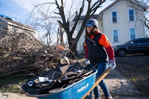 A volunteer in orange wheeling debris from property of home.