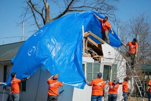 A group of volunteers putting blue tarp on roof of house.