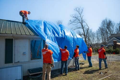 A group of volunteers putting blue tarp on roof of house.