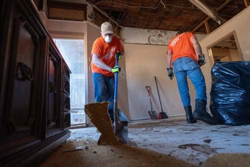 Two volunteers in orange removing flooring in homeowner's house.