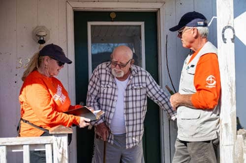 Two volunteers in orange shirts reading the bible to homeowner.