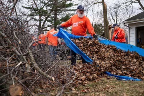 Volunteers removing leaves and debris on blue tarp from yard.