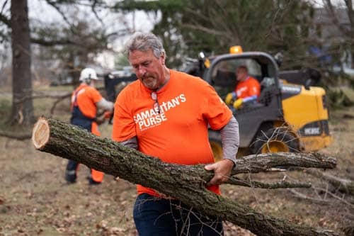 Volunteer in orange shirt carrying large tree log.