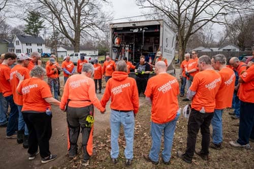Volunteers in orange praying in circle.